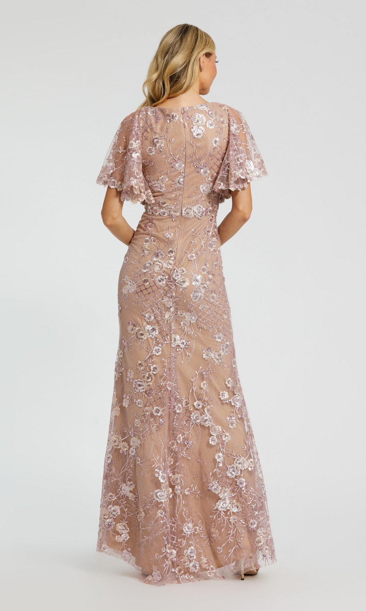 A blonde woman is seen from the back wearing the Mac Duggal 68743 long formal dress in blush pink, featuring flutter sleeves and detailed floral embroidery.